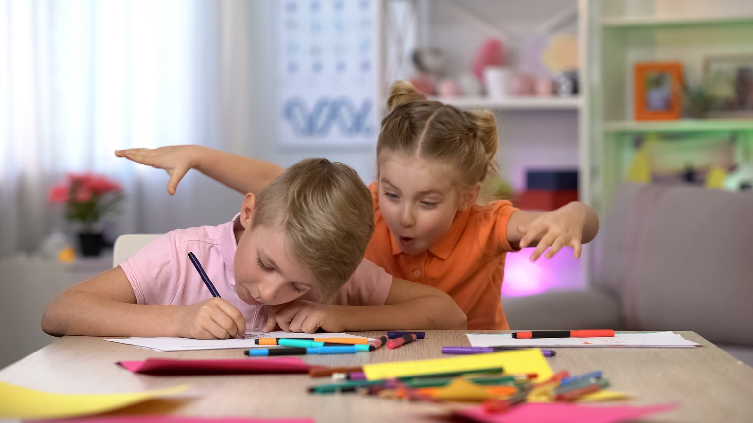 Girl scaring brother studying at table, child hyperactivity, attention deficit